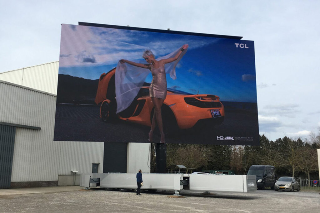 a rotatable mobile LED screen semi open trailer screen test at our manufacturing facility - woman in front of orange sports car on screen